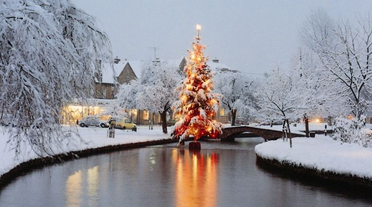 A snow-covered Christmas tree in a river in the middle of a picturesque Cotswold village with fairy lights reflecting on the water. Does it get any more Christmassy than this?